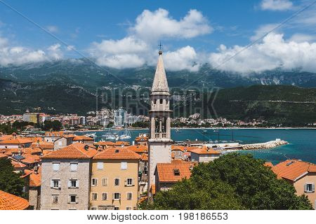 Budva Old town view from above to city roofs, St.John church spire, cloudy mountains and Adriatic sea on background. Tourist capital Budva high view, Montenegro.