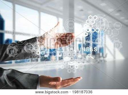 Cropped image of business woman in suit with business interface and media icons in her hands. Office view on background. Mixed media.