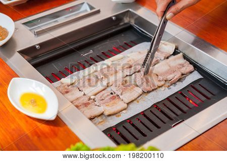 Process Of Cooking Korean Barbecue Raw Pork On The Tabletop Grill In Restaurant. Selective Focus. Cl