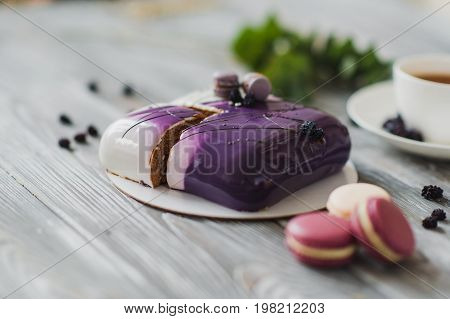 Traditional purple berry cake and macarons souffle dessert and almond dacquoise, raspberry confit, crispy layer with caramelized hazelnuts and raspberry powder, mousse based on bitter chocolate served on wooden table background. Rustic style and natural l