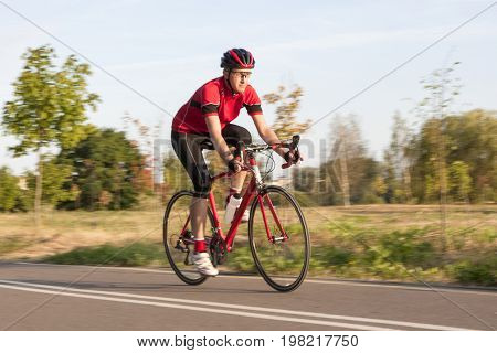 Cycling Concepts. Professional Male Cyclist in Racing Outfit During a Ride on Bike Outdoors. Panning Technique Used. Horizontal Image Composition