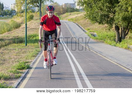 Sport and Cycling Ideas. Portrait of Professional Male Cyclist Doing Uphill on Road Bike. Fully Equipped in Professional Outfit. Horizontal Image