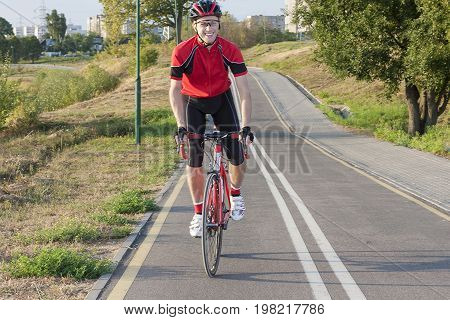 Sport and Cycling Ideas. Portrait of Professional Male Cyclist Doing Uphill Out of the Saddle on Road Bike. Fully Equipped in Professional Outfit. Horizontal Image