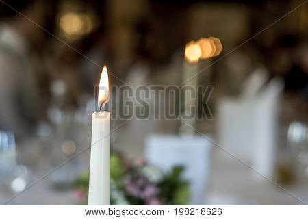 Closeup of a burning white candle romantic dinner table memory memorial in front of bokeeh background