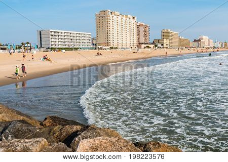 VIRGINIA BEACH, VIRGINIA - JULY 13, 2017:  View of boardwalk hotels and people enjoying the beach as seen from the oceanfront jetty.