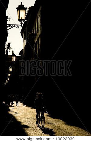 Sepia tonet gamle gade i Padova, Italien, med silhuet af cyklist og baggrundsbelyst gamle lightpost