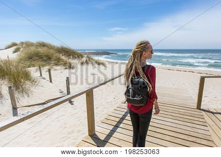 Young beautiful blonde girl with the dreads is on the path to the ocean.