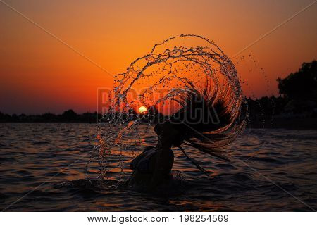 Beautiful young woman throwing back her hair into the water at the beach. Happy girl on the sea. Summer vacation concept