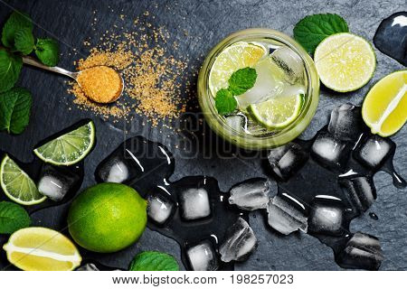 Refreshing mint cocktail mojito with rum and lime, cold drink or beverage with ice on black background, top view