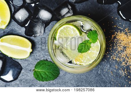 Refreshing mint cocktail mojito with rum and lime, cold drink or beverage with ice on black background, top view