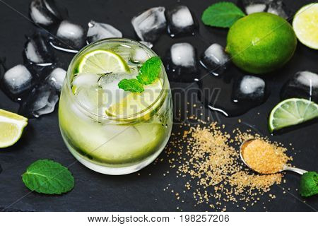 Refreshing mint cocktail mojito with rum and lime, cold drink or beverage with ice on black background, top view