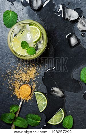 Refreshing mint cocktail mojito with rum and lime, cold drink or beverage with ice on black background, top view