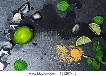 Refreshing mint cocktail mojito ingredirnts, cold drink or beverage with ice on black background, top view