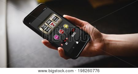 Slot machine with text and numbers on mobile display against cropped hand of woman holding phone in kitchen