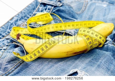Jeans belt loops and pocket close up. Banana wrapped with yellow measure tape on jeans white background. Health and male sexuality concept. Mens denim pants with banana imitating male genitals.