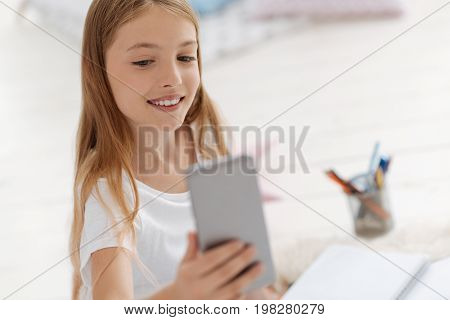 One more shot. Selective focus on an adorable girl grinning while holding a smartphone and posing for self portraits for he social media mage.