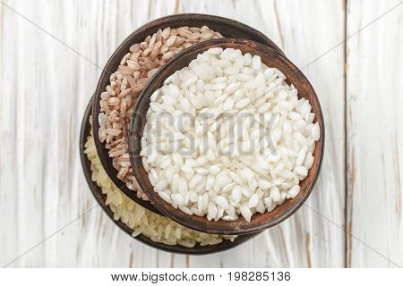 Set various organic raw rice on a wooden white table in ceramic bowls. Devzira. Arborio. Selective focus
