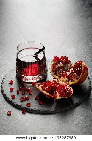 Delicious, organic and healthful pomegranate juice in a fancy glass and a garnet grain on a black tray on a light gray background. Healthful bittersweet beverage and nutritious garnet seeds.
