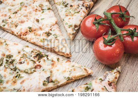 Pizza and cherry tomatoes on a branch on a light wooden background