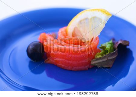 Slice of salmon with lemons and olives on a plate.
