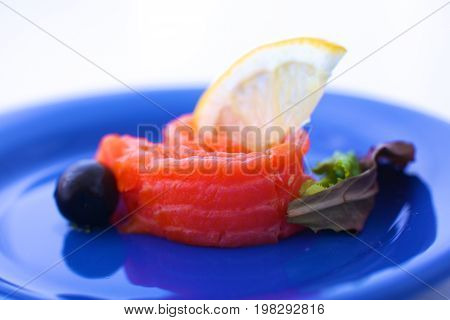 Slice of salmon with lemons and olives on a plate.