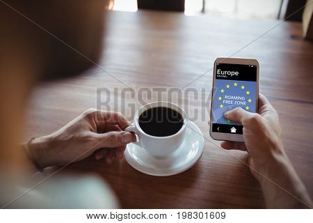 Roaming free zone text and European Union flag on mobile screen against man using mobile phone while having coffee