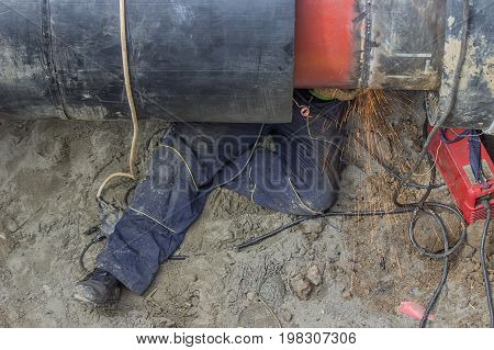 Welder Worker Grinding The Weld In Trench Under Pipeline