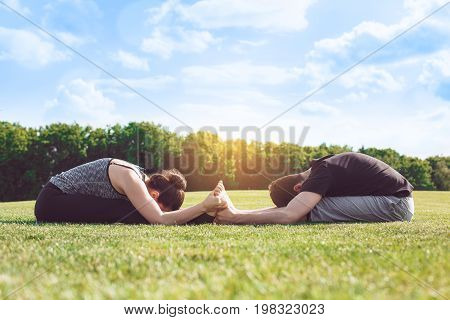 Man and woman practice acro yoga in the park stretching