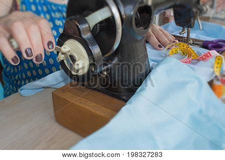 woman seamstress sitting and sews on sewing machine. Dressmaker work on the sewing machine. Tailor making a garment in her workplace. Hobby sewing as a small business concept