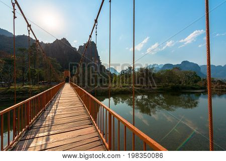 Picture of orange bridge over the Nam Song River with tropical vegetation. Close to Tham Chang Cave in the city of Vang Vieng Laos.