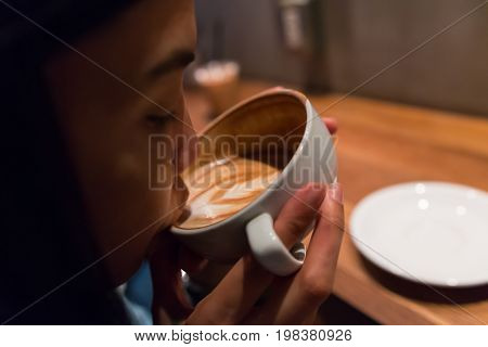 a girl is sipping the hot latte coffee in the morning