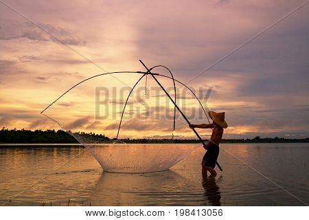 Fisherman on silhouette sunrise with gear fishing on the lake is a culture of Thai or Laos people's