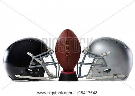 Close up of American football on tee by sports helmets against white baclground
