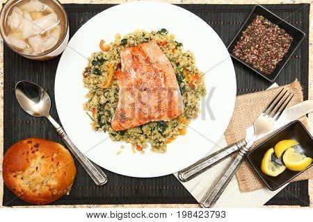 Salmon with Cracked Freekeh Salad at table with spicy salsa verde, iced tea, lemon and an onion roll.