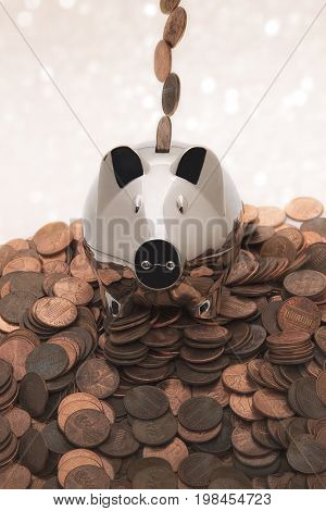 A chrome piggy bank on a pile of pennies with pennies coming down from above going into the coin slot.