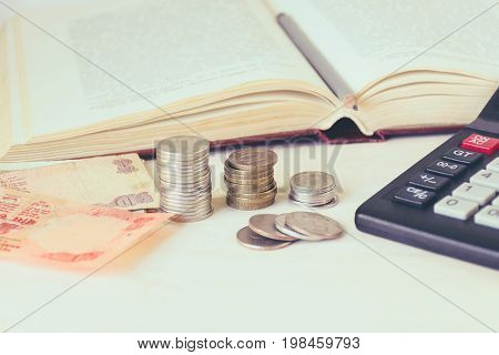 Money banknote coins in piles a calculator in front of an open book. The concept of expensive education and low scholarship. Toned image