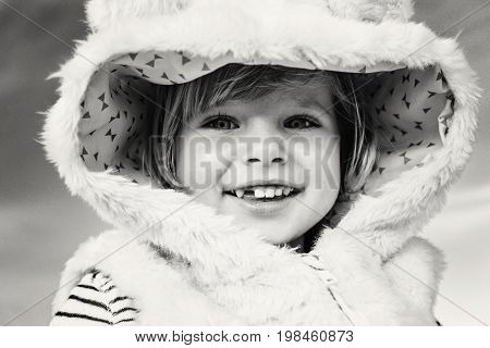 Closeup black-and-white portrait of cute adorable funny smiling laughing Caucasian kid baby girl in fur coat looking in camera. Happy lifestyle childhood concept. Child with missing tooth