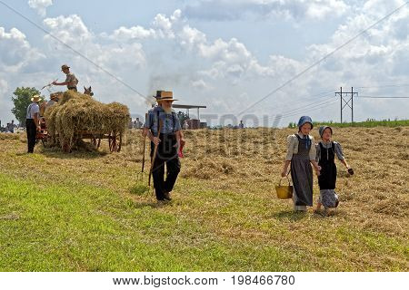 NEW HOLLAND PENNSYLVANIA - August 4 2017: Two young Mennonite girls with a pail and cup carry water for the hay crew at Big Spring Farm Days. This is an annual event demonstrating traditional threshing and harvesting methods using restored antique and vin