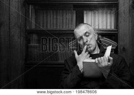 Man reading interesting book against the bookshelf in black and white