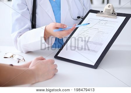 Close up of a doctor and  patient hands while phisician pointing into medical history form at clipboard. Medicine and health care concept