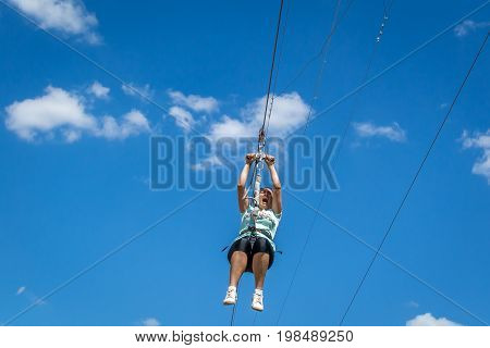 Ukraine Migea - July 30 2017: Zipline. A view of a man sliding on a steel cable against a beautiful blue sky with white clouds. Emotion of delight. Extreme and active rest.