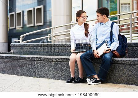 Portrait of happy teenage couple chatting outside of school building during break