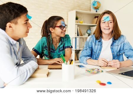 Group of children playing guessing game at table in classroom with names on their heads