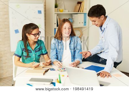 Portrait of three school children preparing for seminar together, discussing project at table in class