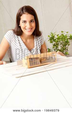 En ung kvindelig arkitekt smiler til kameraet med et hus model