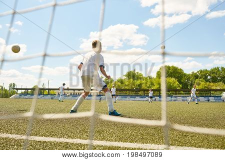 Back view portrait of teenage goalkeeper protecting gate during junior football match or practice, shot from behind gate net