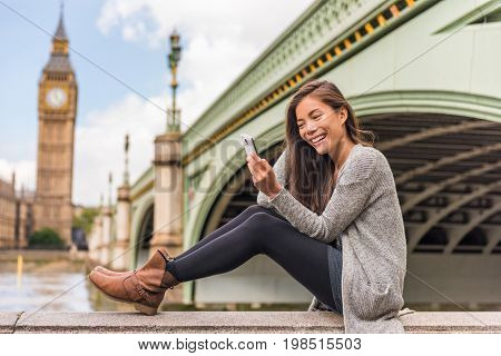 London urban people city lifestyle woman using phone app texting sms on social media. Young Asian girl holding cellphone at Westminster bridge, Big Ben Houses of Parliament background.