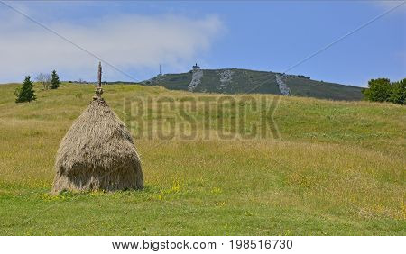 The Matajur mountain in Friuli Venezia Giulia Italy. The rounded hill with the church in the background is the peak of the Matajur. A loose stacked haystack can be seen in the foreground