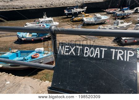 Boats beached in the mud in harbor as a sign announces next boat trip