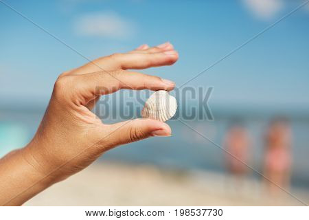 Little Beautiful Sea Shell In Woman`s Hands Against Beutiful Marine Background. Woman Having Holiday